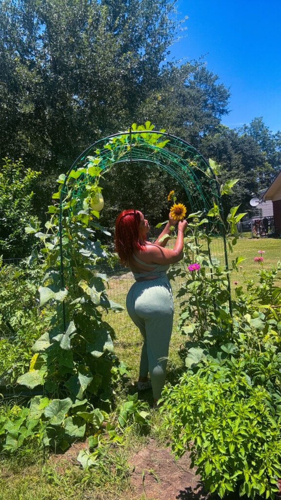 Allyse standing beneath a lush garden arch with climbing vines and sunflowers