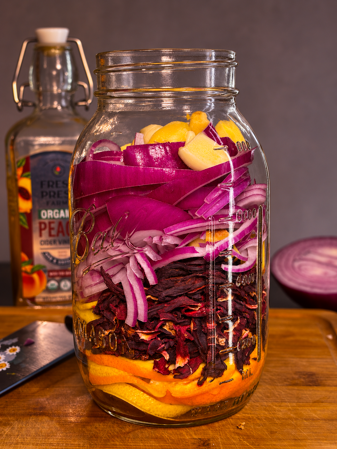 Mason jar packed with hibiscus fire cider ingredients including red onion, ginger, garlic, citrus, and roselle